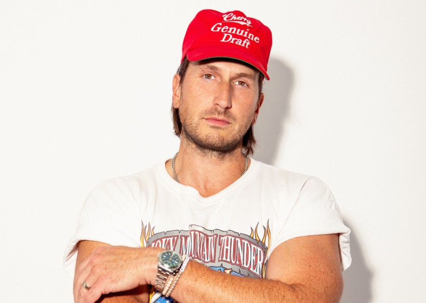 A man in a white graphic tshirt and red cap stood in front of a white wallx